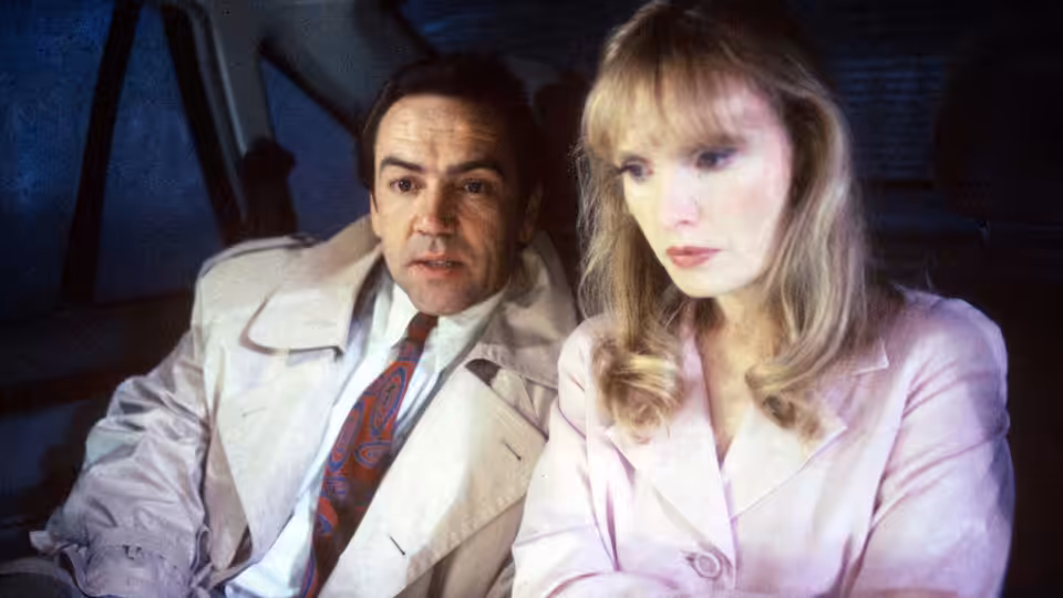 Robert Lindsay as Michael Murray seated beside a blonde woman in pink