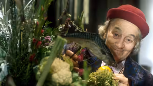 Man in red hat holding a fish among vegetables and smiling