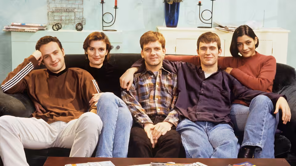Five young adults sitting closely together on a black sofa