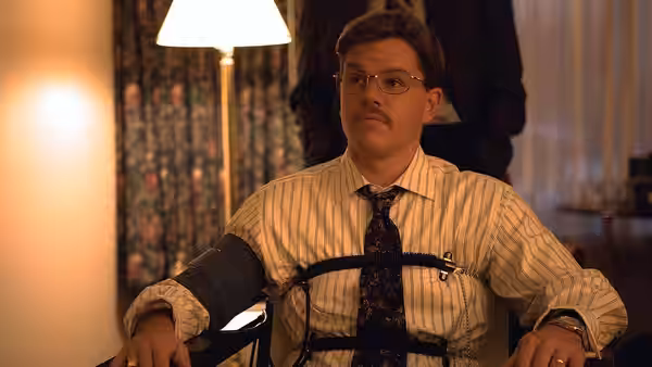 Mark Whitacre (Matt Damon) wearing a blood pressure cuff while seated indoors