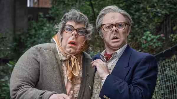 Woman in tweed jacket and headscarf stands beside suited man outdoors with shocked expressions