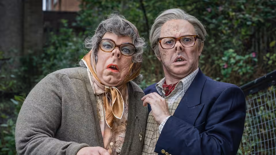 Woman in tweed jacket and headscarf stands beside suited man outdoors with shocked expressions
