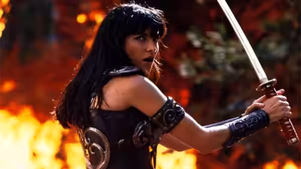 Xena (Lucy Lawless) gripping a sword while turning in a burning landscape