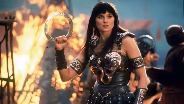 Xena (Lucy Lawless) holding up her chakram with flames and soldiers behind