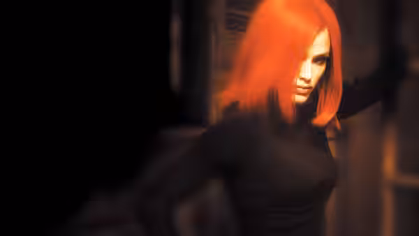 Woman with bright red hair moves through a dimly lit industrial hallway