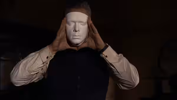 A man holding a white mask over his face with both hands