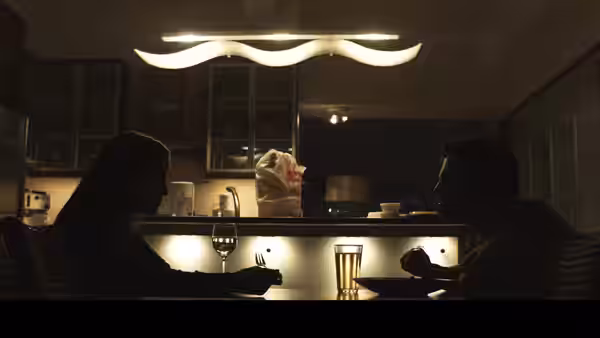 a woman and a man seated at a kitchen counter with wine glasses