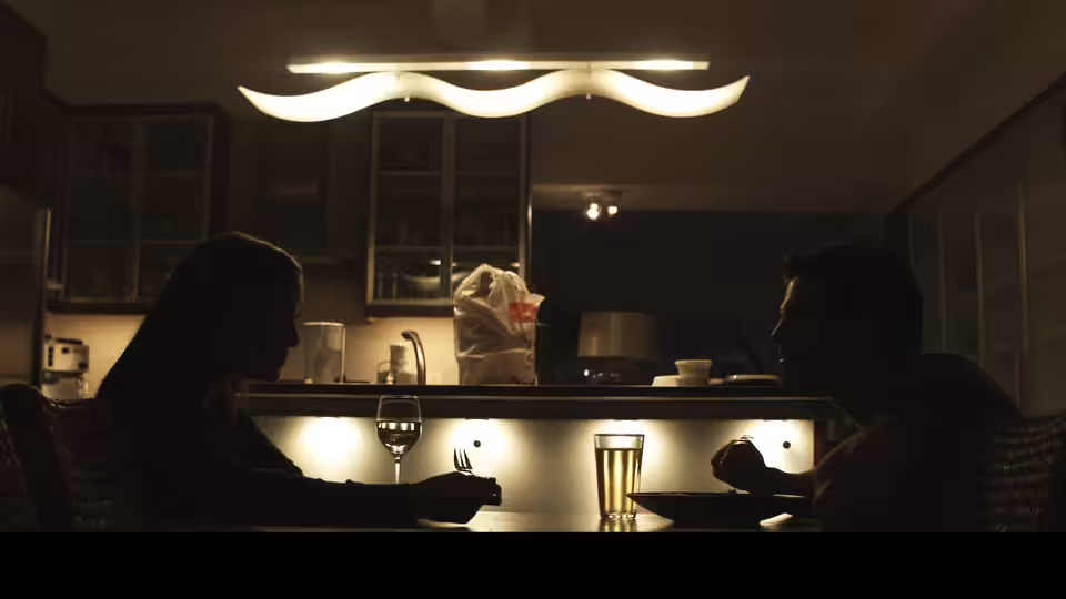 a woman and a man seated at a kitchen counter with wine glasses