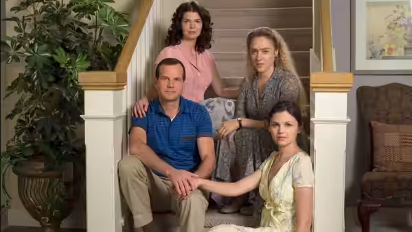 Man seated on stairs with three women around him indoors