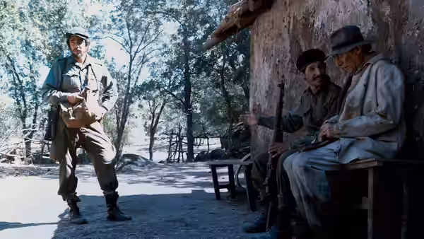 Che Guevara (Benicio del Toro) standing before two seated men with rifles