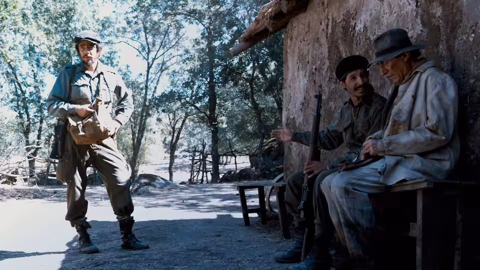 Che Guevara (Benicio del Toro) standing before two seated men with rifles