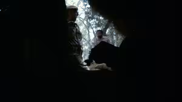 Two men in military attire conversing at the entrance of a dark shelter