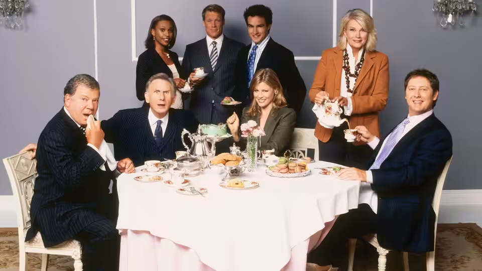 Lawyers in suits gathered around a table set with cakes and tea