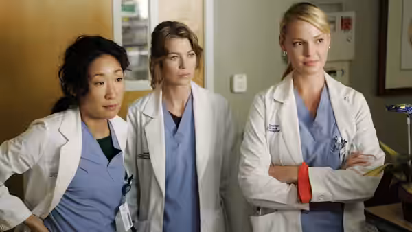 Cristina Yang (Sandra Oh), Meredith Grey (Ellen Pompeo) and Izzie Stevens (Katherine Heigl) standing in a hospital corridor
