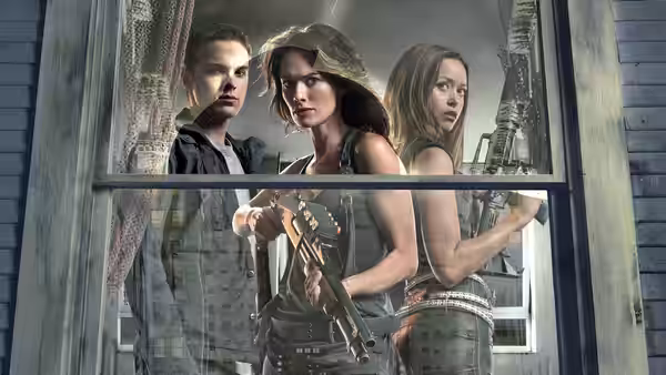 Sarah Connor holding a rifle by a broken window with two companions