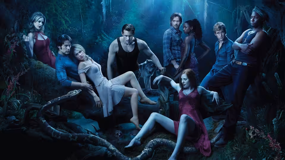 Group of people gathered around a woman reclining on a tree in a forest