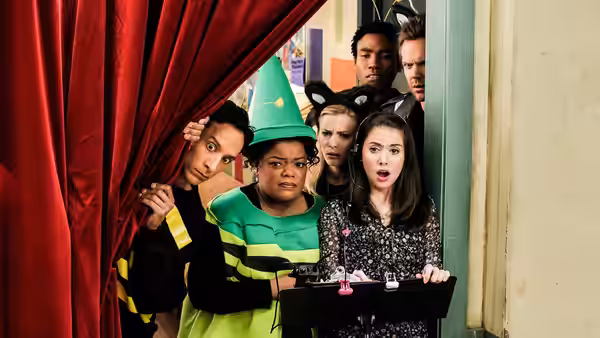 Annie (Alison Brie) holds a tray while costumed friends peer from behind a red curtain