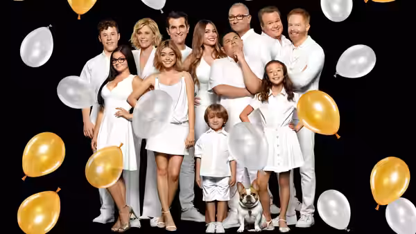 Adults and children in white outfits pose with balloons against a black backdrop