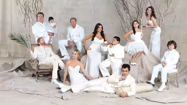 Adults and children in white clothing pose among branches and draped fabric