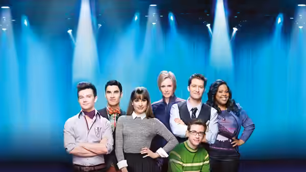 Seven young adults posing together under blue spotlights on a stage