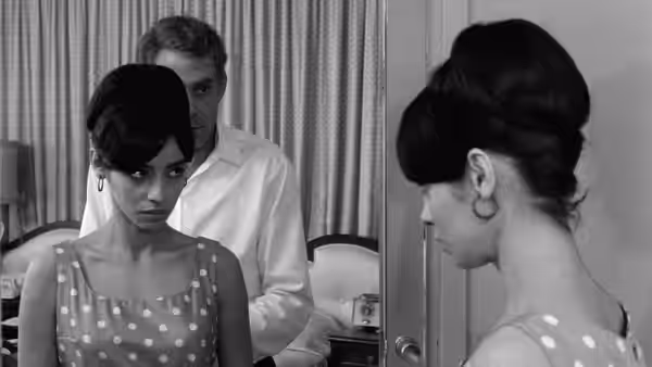 Two women stand in a room as a man watches from behind them