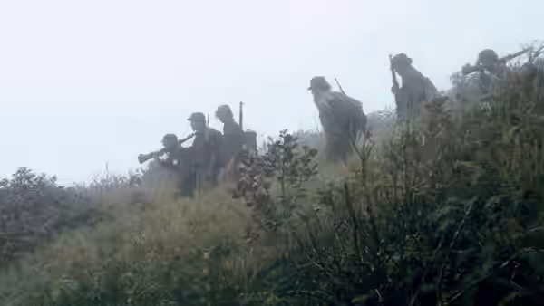 A group of armed rebels climbing a grassy hillside in fog
