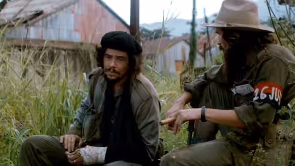 Ernesto Che Guevara (Benicio del Toro) sitting on the ground beside another fighter