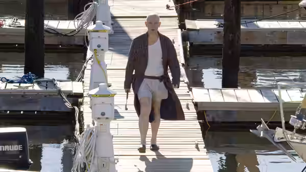 Osborne Cox (John Malkovich) walks along a marina dock in a robe and underwear