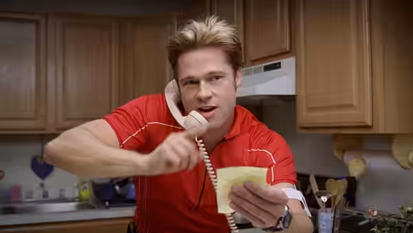 Chad Feldheimer (Brad Pitt) reads a note while talking on a cordless phone in a kitchen