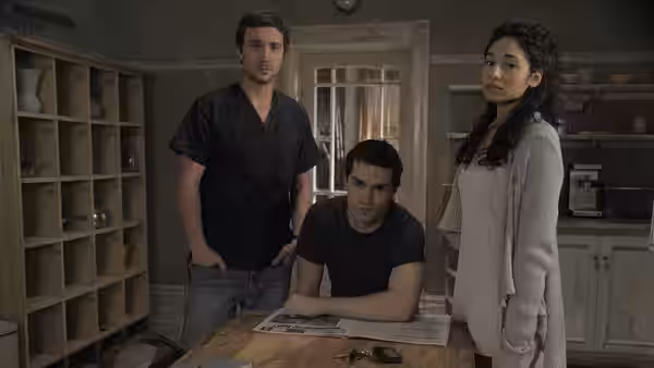 Aidan Waite (Sam Witwer) seated at table with Josh Levison (Sam Huntington) and Sally Malik (Meaghan Rath) in kitchen