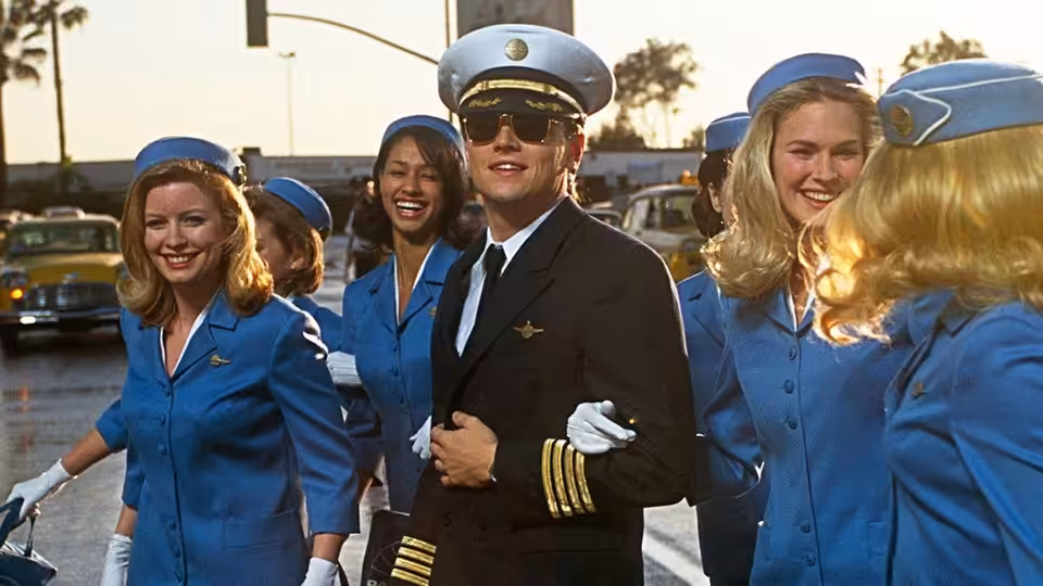 Frank Abagnale Jr. (Leonardo DiCaprio) smiling among flight attendants on the tarmac
