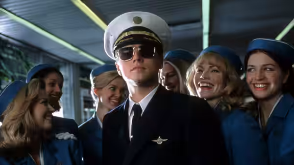 Frank Abagnale Jr. (Leonardo DiCaprio) in pilot uniform surrounded by smiling flight attendants