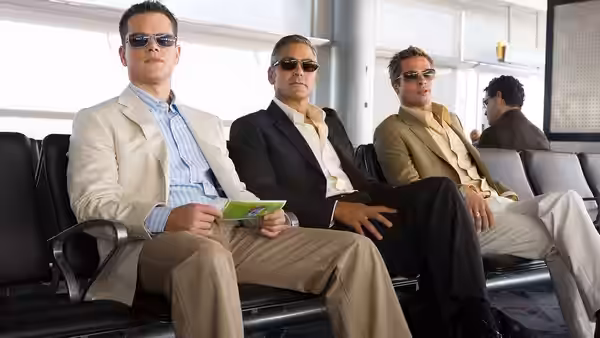 Danny Ocean (George Clooney), Rusty Ryan (Brad Pitt) and Linus Caldwell (Matt Damon) seated in an airport terminal