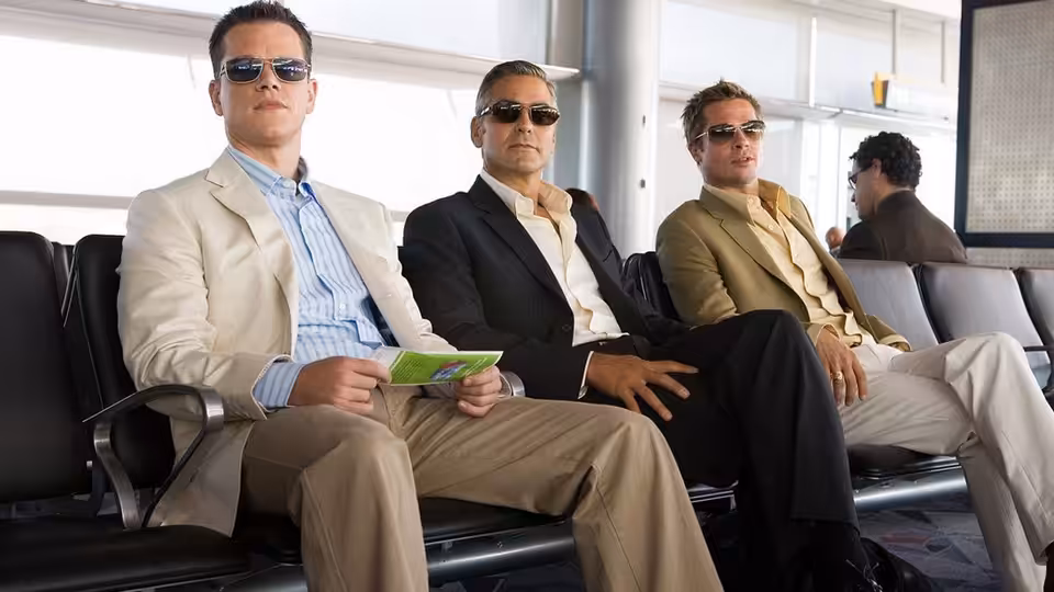 Danny Ocean (George Clooney), Rusty Ryan (Brad Pitt) and Linus Caldwell (Matt Damon) seated in an airport terminal