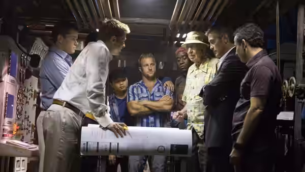 Several men examining large blueprints spread across a table in a workshop