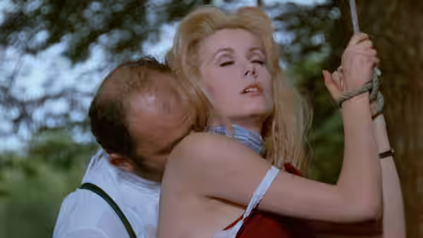 A man embraces Séverine (Catherine Deneuve) outdoors as she holds a rope