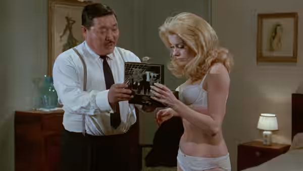 Séverine (Catherine Deneuve) examines a small box as a man in suspenders shows it to her