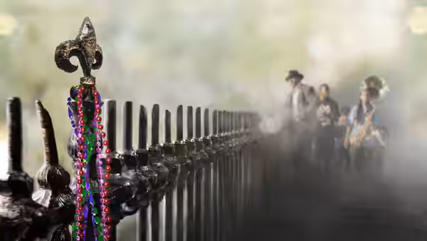 Mardi Gras Indians walking past a fence hung with colorful beads