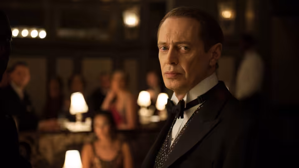 Nucky Thompson (Steve Buscemi) in a tuxedo standing in a crowded restaurant