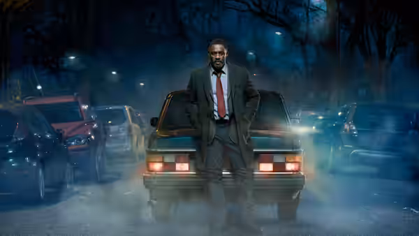John Luther (Idris Elba) stands before a car on a foggy night street