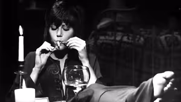 Bree Daniels (Jane Fonda) lights a cigarette at a table beside a candle
