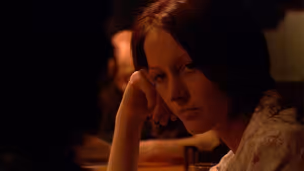 Young woman rests her head on her hand while seated in a dim restaurant
