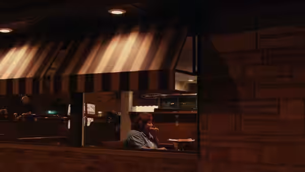 Woman sits alone at a table outside a closed building at night