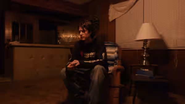 Young man in a hoodie sits in an armchair in a living room