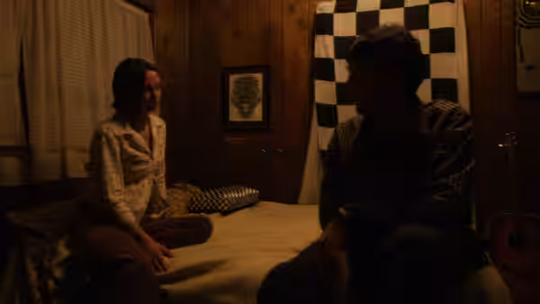 Young woman and young man sit facing each other on a bed in a bedroom