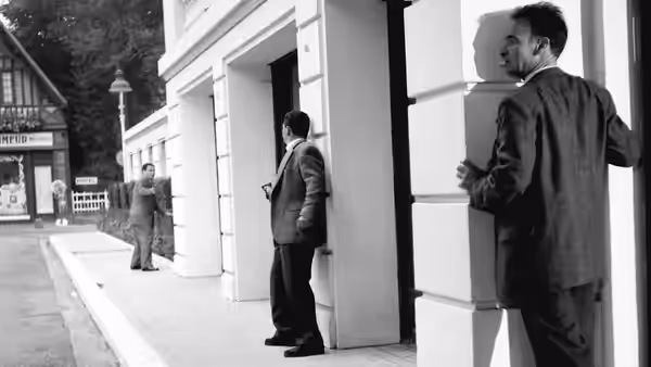 Men stand spaced along the columns of a building exterior
