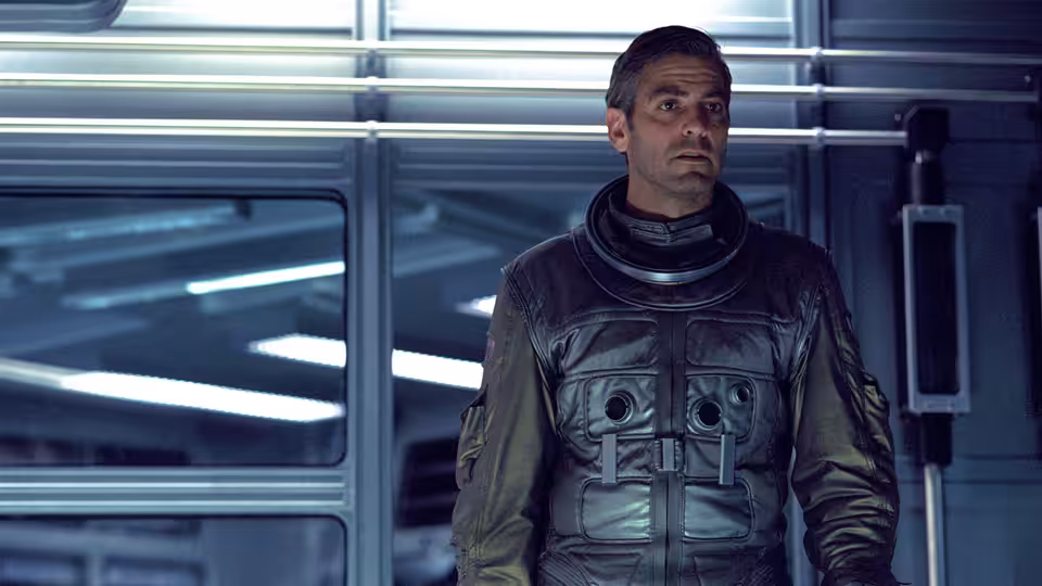 Chris Kelvin (George Clooney) standing in a blue-lit spaceship corridor