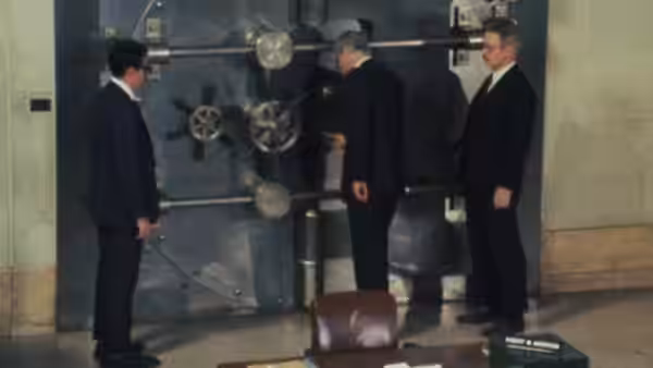Three suited men stand beside a large bank vault door