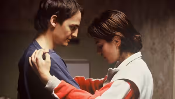 Rosetta (Émilie Dequenne) rests her hands on a young man's shoulders indoors