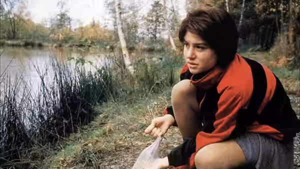 Rosetta (Émilie Dequenne) crouches beside a pond holding a plastic bag